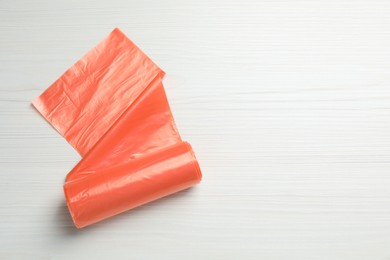 Photo of Roll of orange garbage bags on white wooden table, top view. Space for text