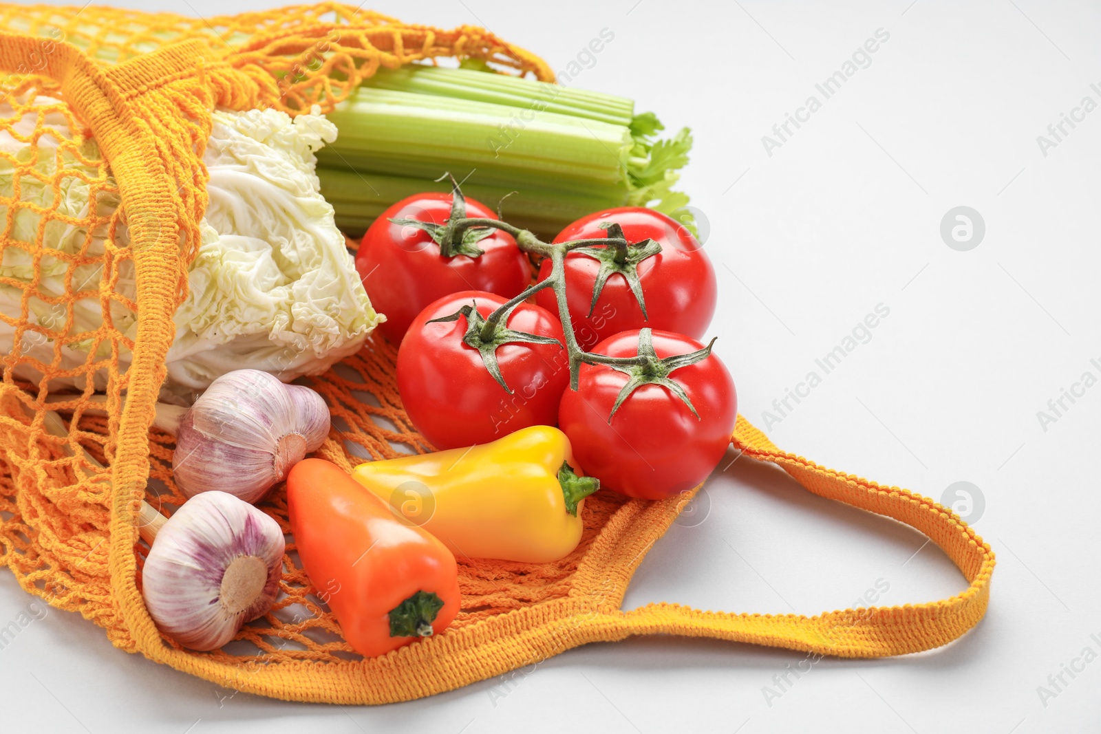 Photo of String bag with different vegetables on light grey background, closeup