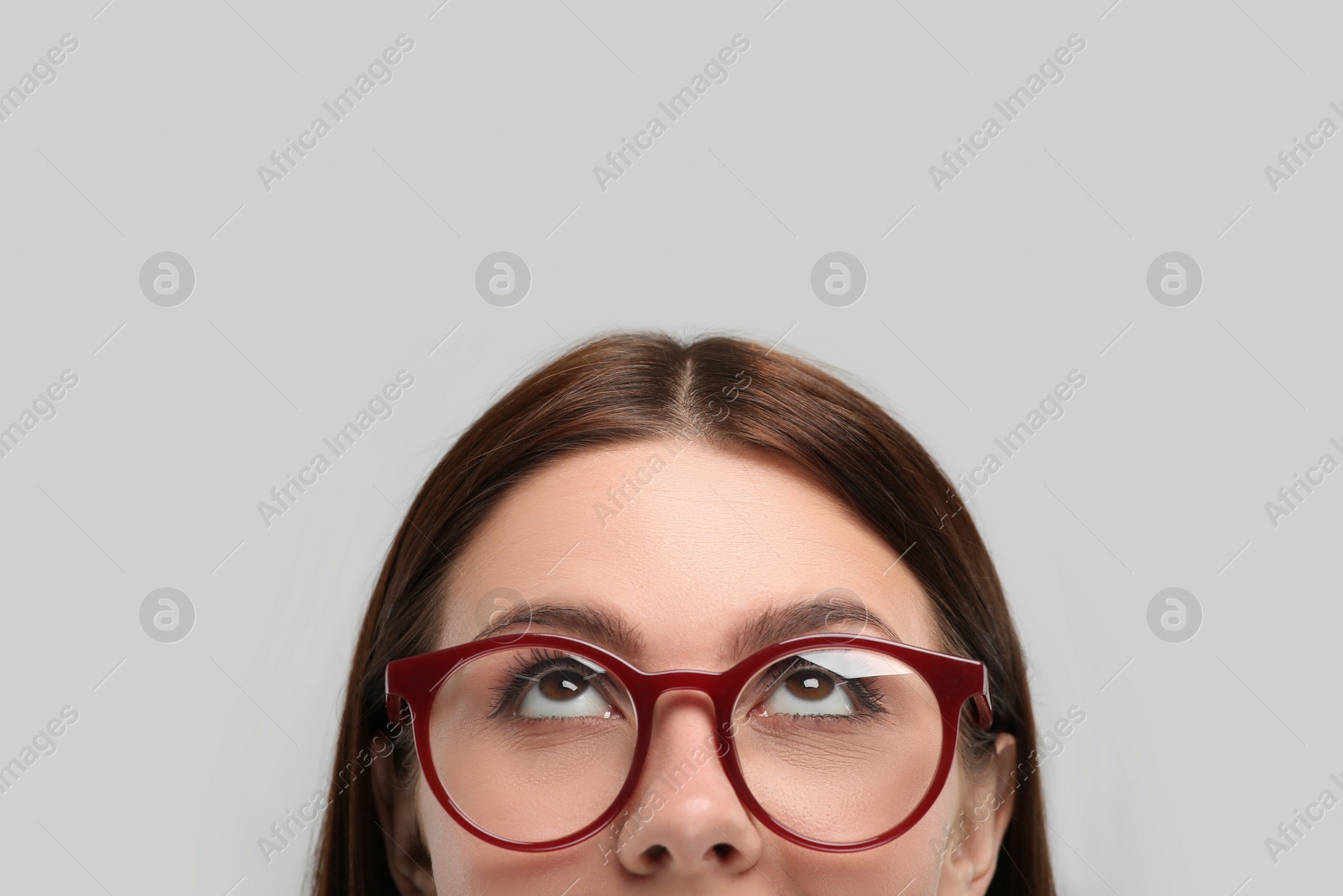 Photo of Woman in stylish eyeglasses looking up on grey background, closeup. Space for text