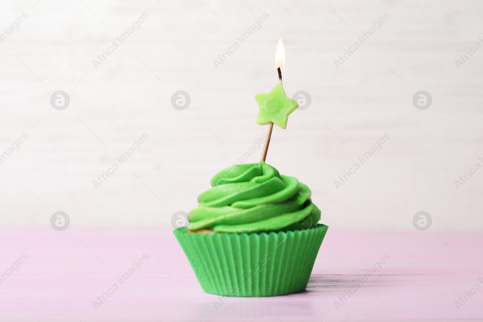 Photo of Delicious birthday cupcake with cream and burning candle on pink table.