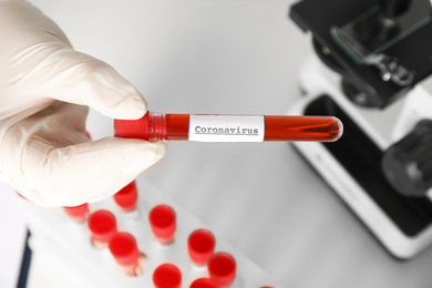 Photo of Scientist holding test tube with blood sample and label CORONA VIRUS in laboratory, above view