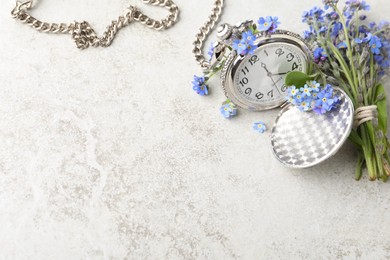 Photo of Beautiful blue forget-me-not flowers with pocket watch on light stone table, flat lay. Space for text