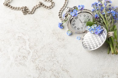 Beautiful blue forget-me-not flowers with pocket watch on light stone table, flat lay. Space for text