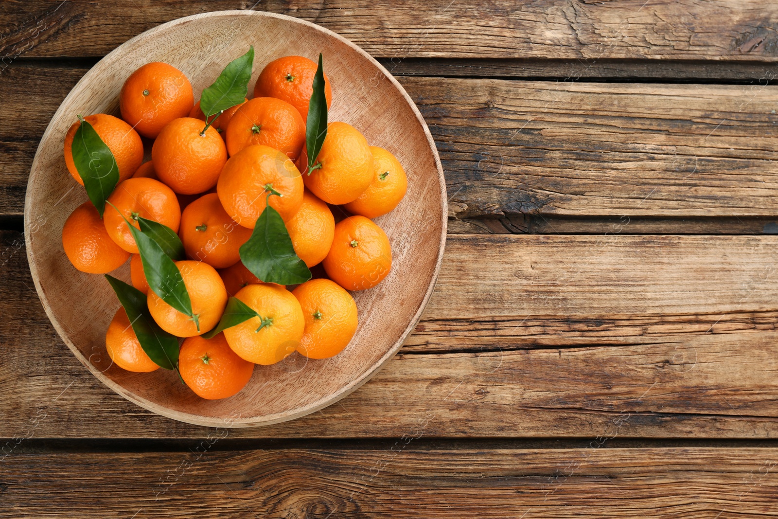 Photo of Fresh ripe tangerines with green leaves on wooden table, top view. Space for text