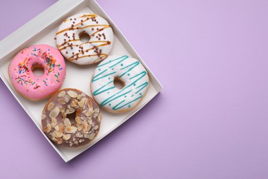 Photo of Box with different tasty glazed donuts on violet background, top view. Space for text