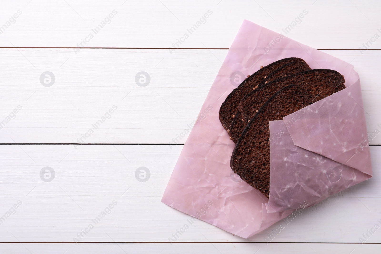 Photo of Bread slices in pink beeswax food wrap on white wooden table, top view. Space for text