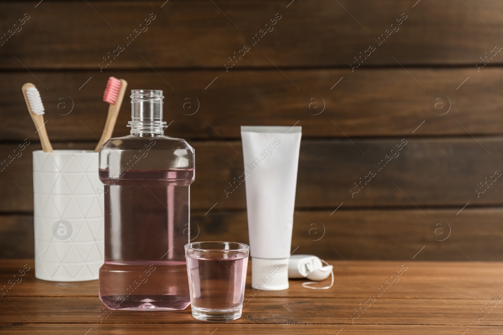 Photo of Bottle and glass with mouthwash near other oral hygiene products on wooden table, space for text