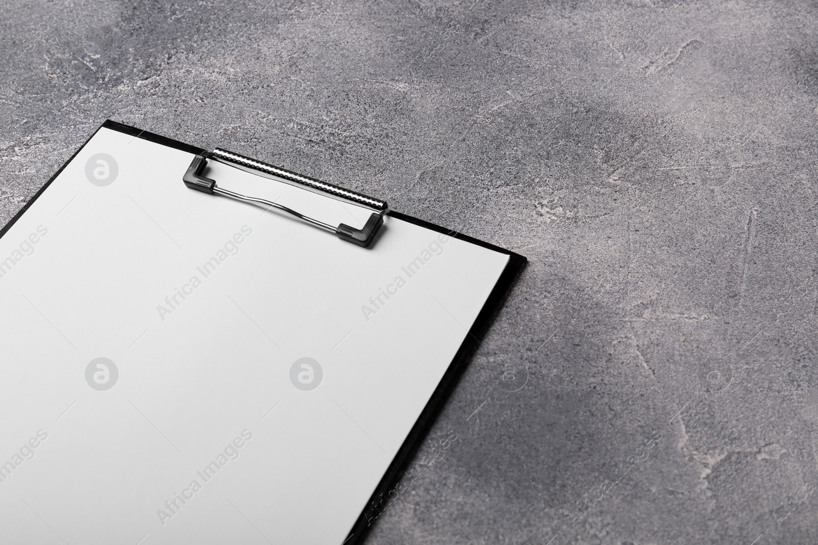 Photo of New clipboard with sheet of blank paper on grey textured table. Space for text