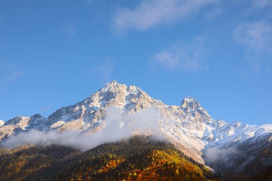 Picturesque landscape of high mountains covered with thick mist under blue sky on autumn day