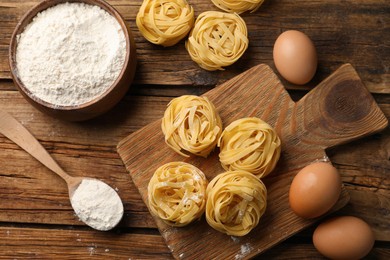 Photo of Uncooked homemade pasta and ingredients on wooden table, flat lay