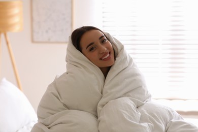 Beautiful young woman wrapped with soft blanket on bed at home