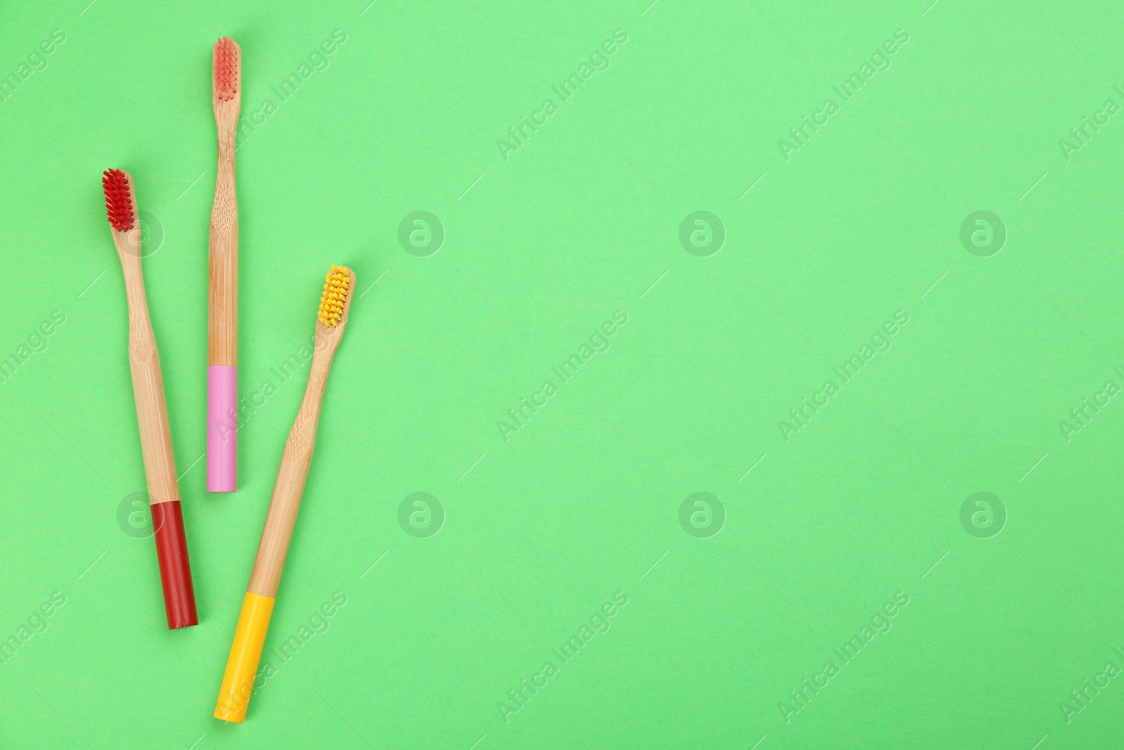 Photo of Natural toothbrushes made with bamboo on green background, flat lay. Space for text