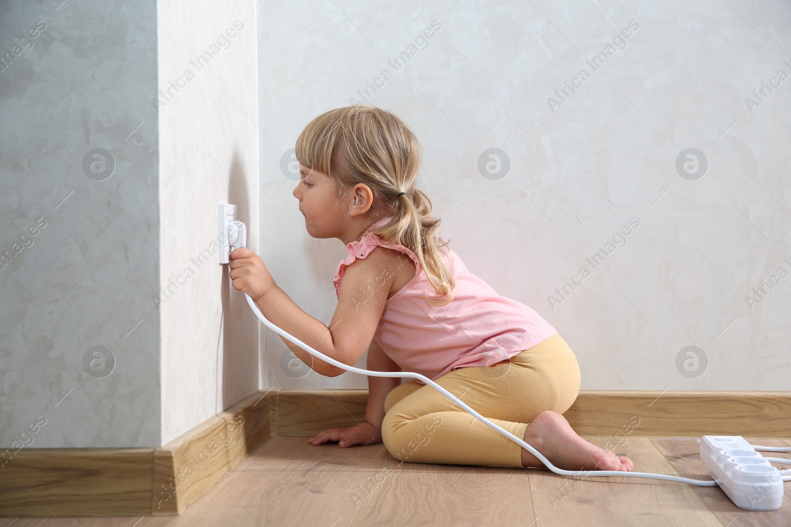 Photo of Little child playing with electrical socket and power strip plug at home. Dangerous situation