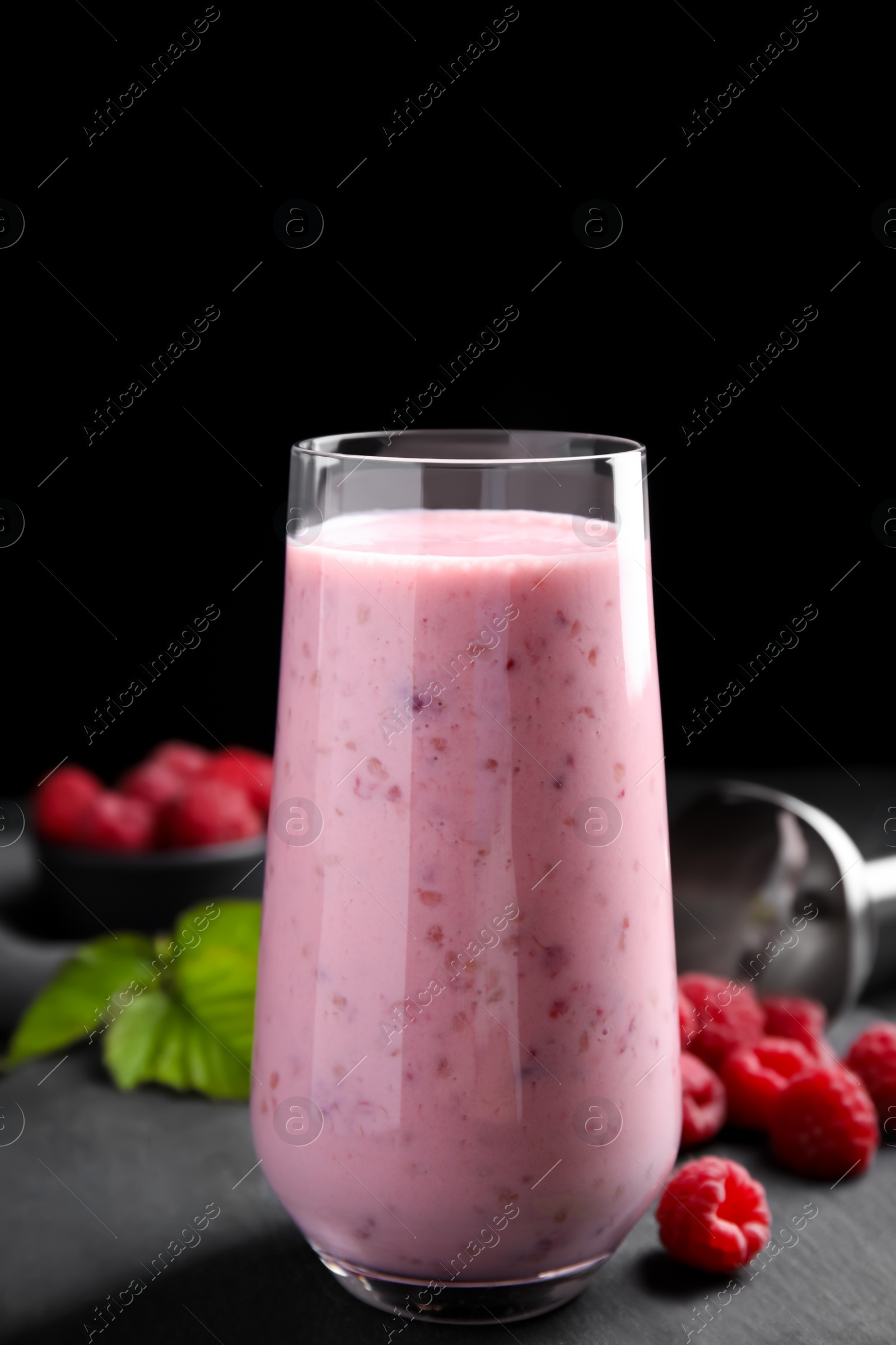 Photo of Glass of tasty raspberry smoothie on dark table against black background