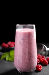 Photo of Glass of tasty raspberry smoothie on dark table against black background