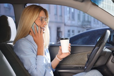 Coffee to go. Happy woman with paper cup of drink talking on smartphone in car