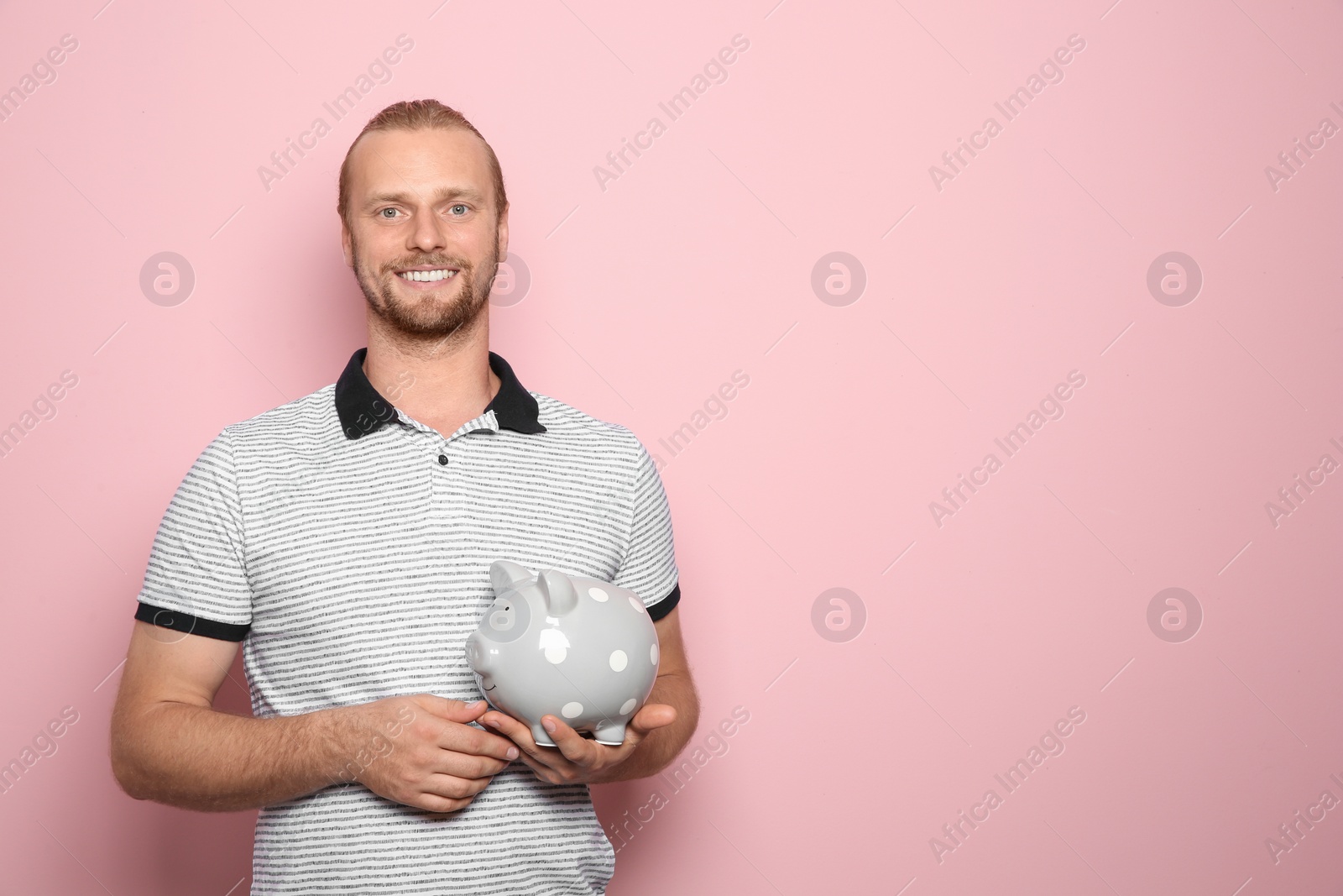 Photo of Happy man with piggy bank on color background. Space for text