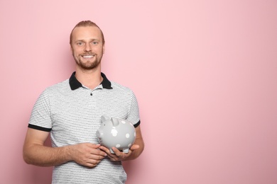 Photo of Happy man with piggy bank on color background. Space for text