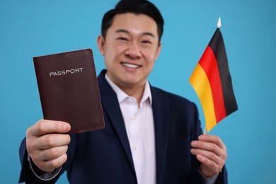 Photo of Immigration. Happy man with passport and flag of Germany on light blue background, selective focus