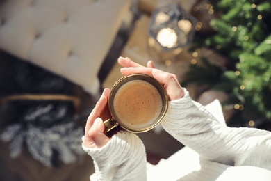 Photo of Woman with golden cup of hot drink in room decorated for Christmas, top view