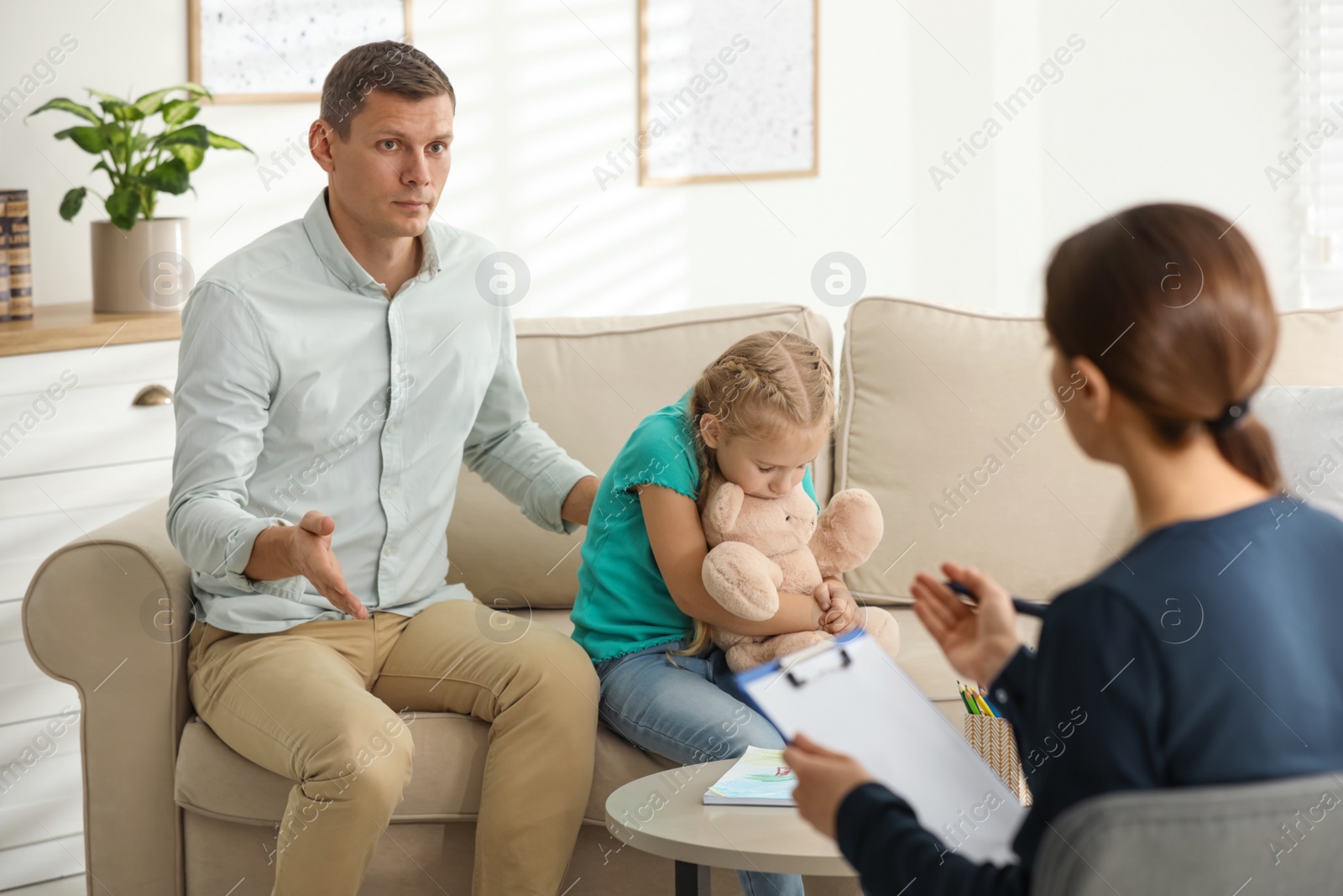 Photo of Little girl and her father on appointment with child psychotherapist indoors