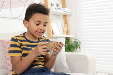 Cute African-American boy playing on phone at home. Space for text