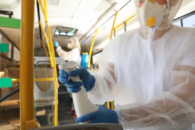 Photo of Public transport sanitation. Worker in protective suit disinfecting bus salon, focus on hand with spray bottle