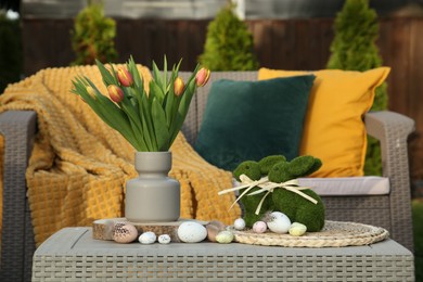 Photo of Terrace with Easter decorations. Bouquet of tulips in vase, bunny figures and decorative eggs on table outdoors