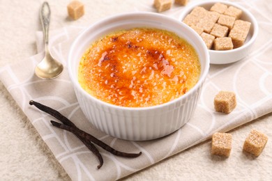 Delicious creme brulee in bowl, vanilla pods and sugar cubes on light textured table, closeup