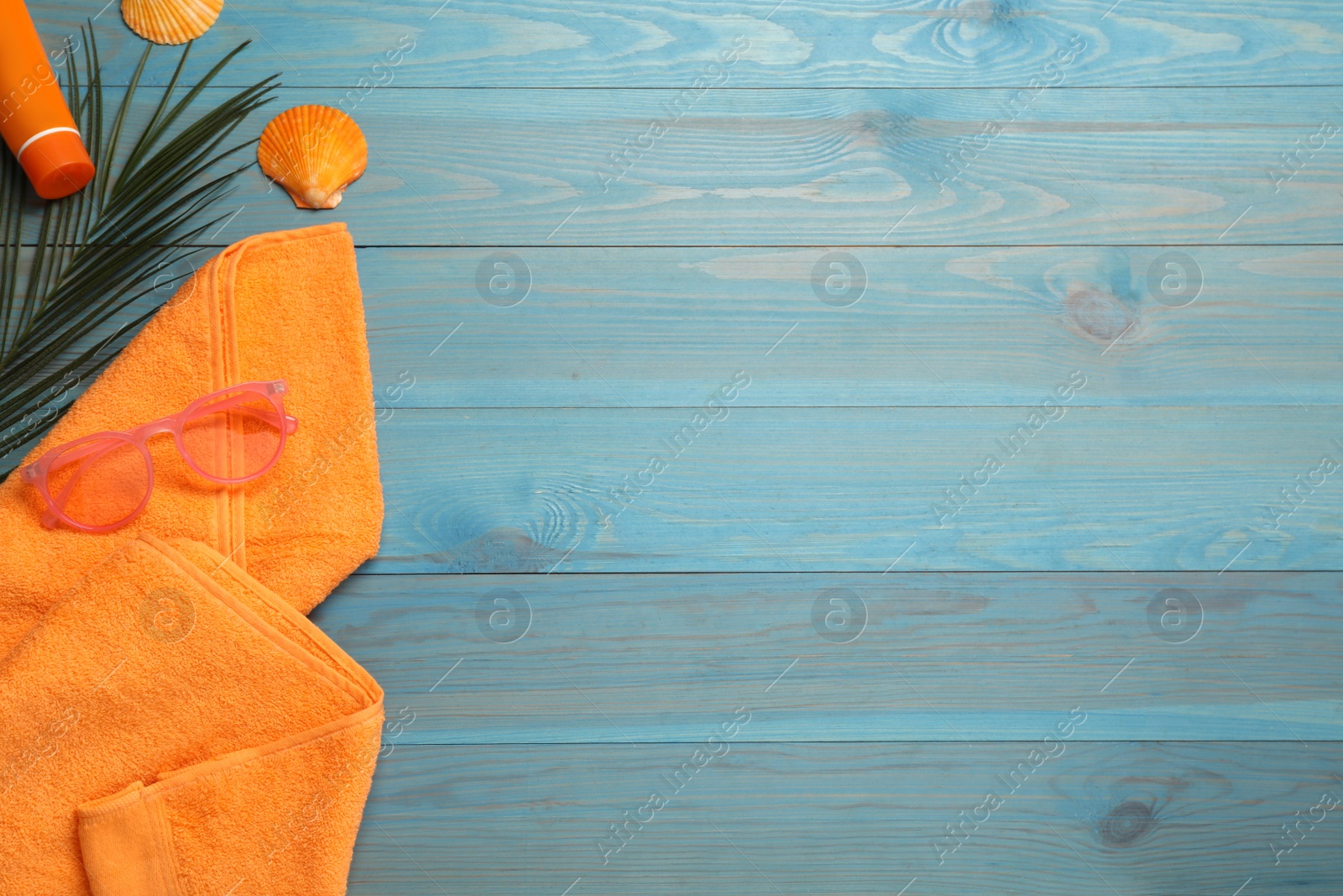 Photo of Beach towel, sunglasses and sun protection product on light blue wooden background, flat lay. Space for text