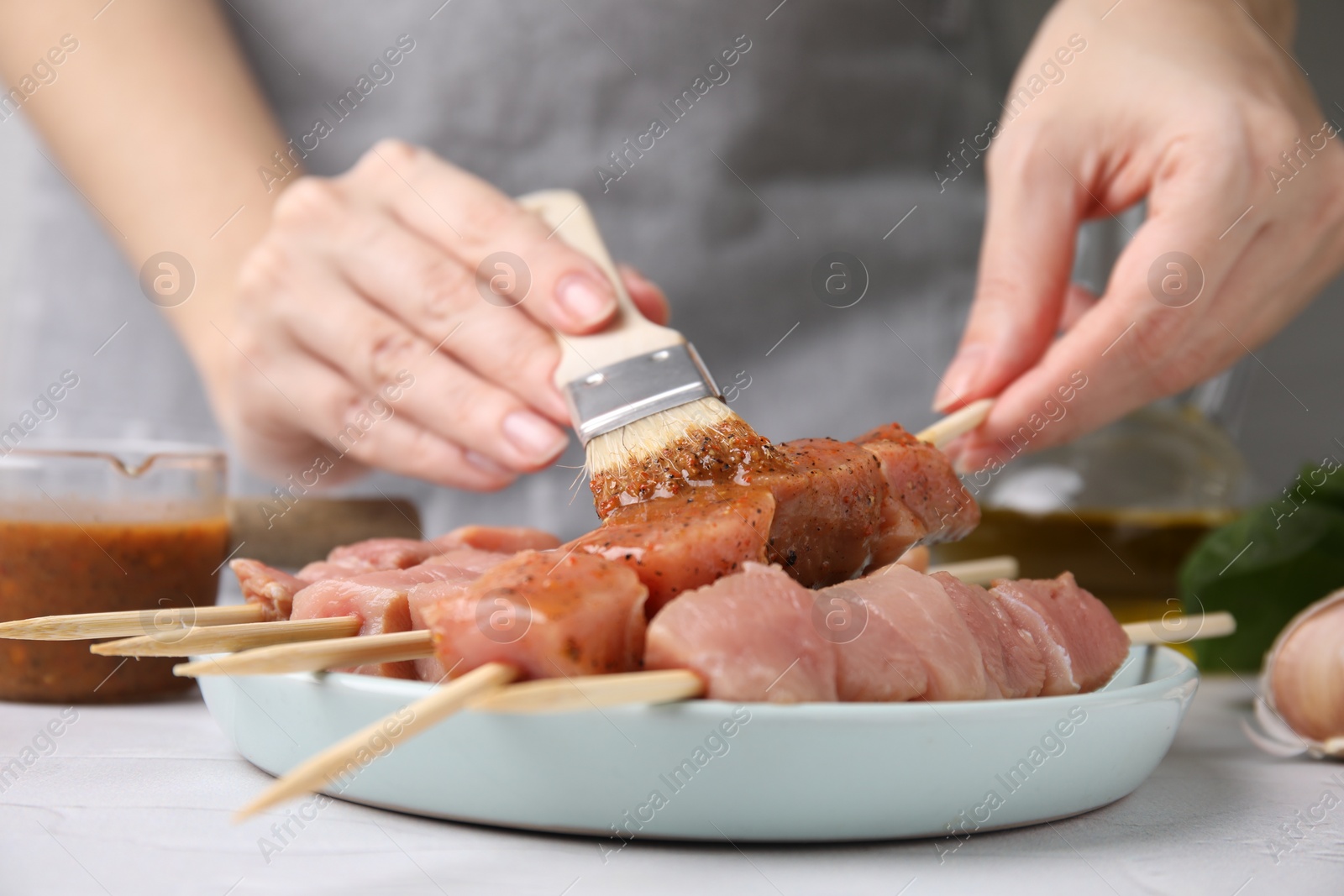 Photo of Woman spreading marinade onto raw meat with basting brush at table, closeup