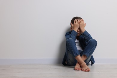 Photo of Child abuse. Upset girl sitting on floor near white wall, space for text