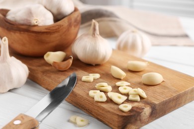 Photo of Aromatic cut garlic, cloves, bulbs and knife on white wooden table, closeup