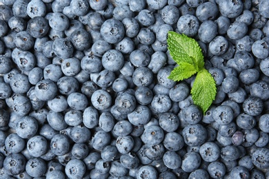 Photo of Juicy fresh blueberries and green leaves as background, top view