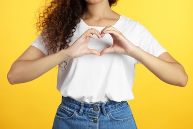 Photo of African-American woman making heart with hands on yellow background, closeup