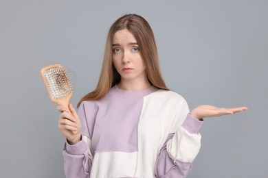 Photo of Upset woman holding brush with lost hair on light grey background. Alopecia problem