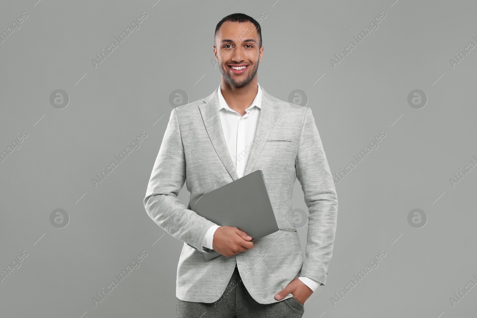 Photo of Young businessman in formal outfit with laptop on grey background