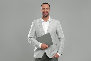 Young businessman in formal outfit with laptop on grey background