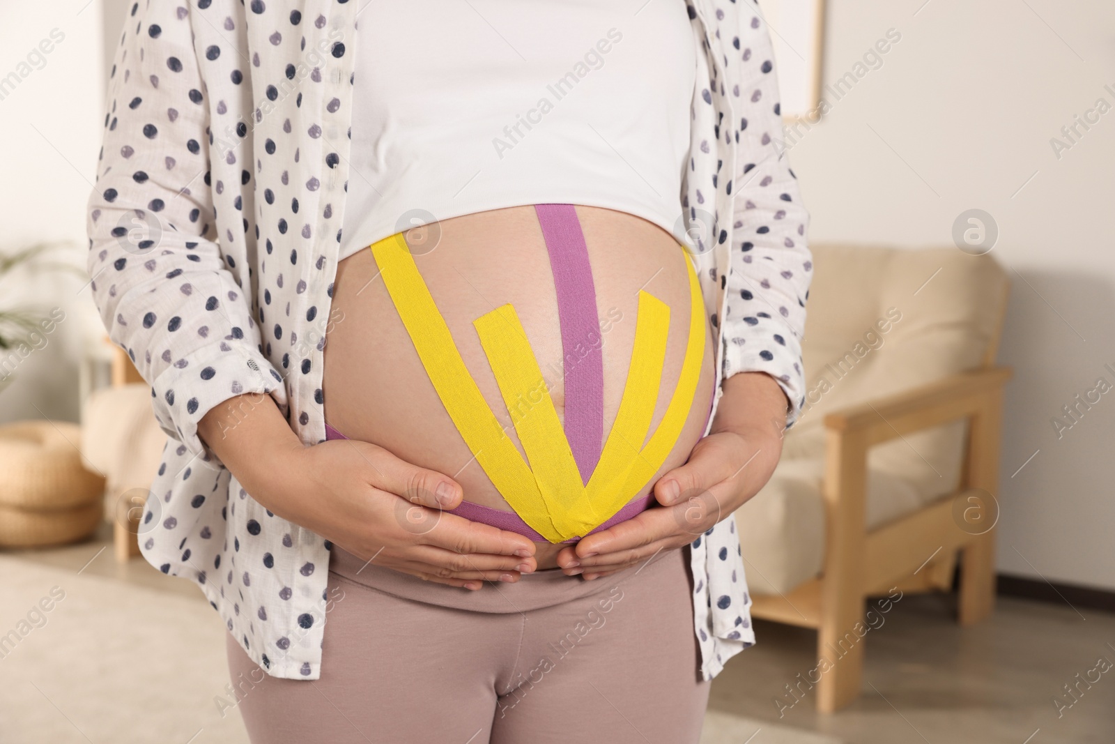 Photo of Pregnant woman with kinesio tapes on her belly at home, closeup