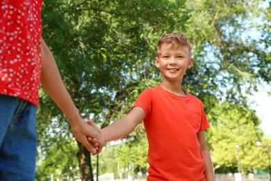 Photo of Little boy and his mother holding hands outdoors. Family weekend