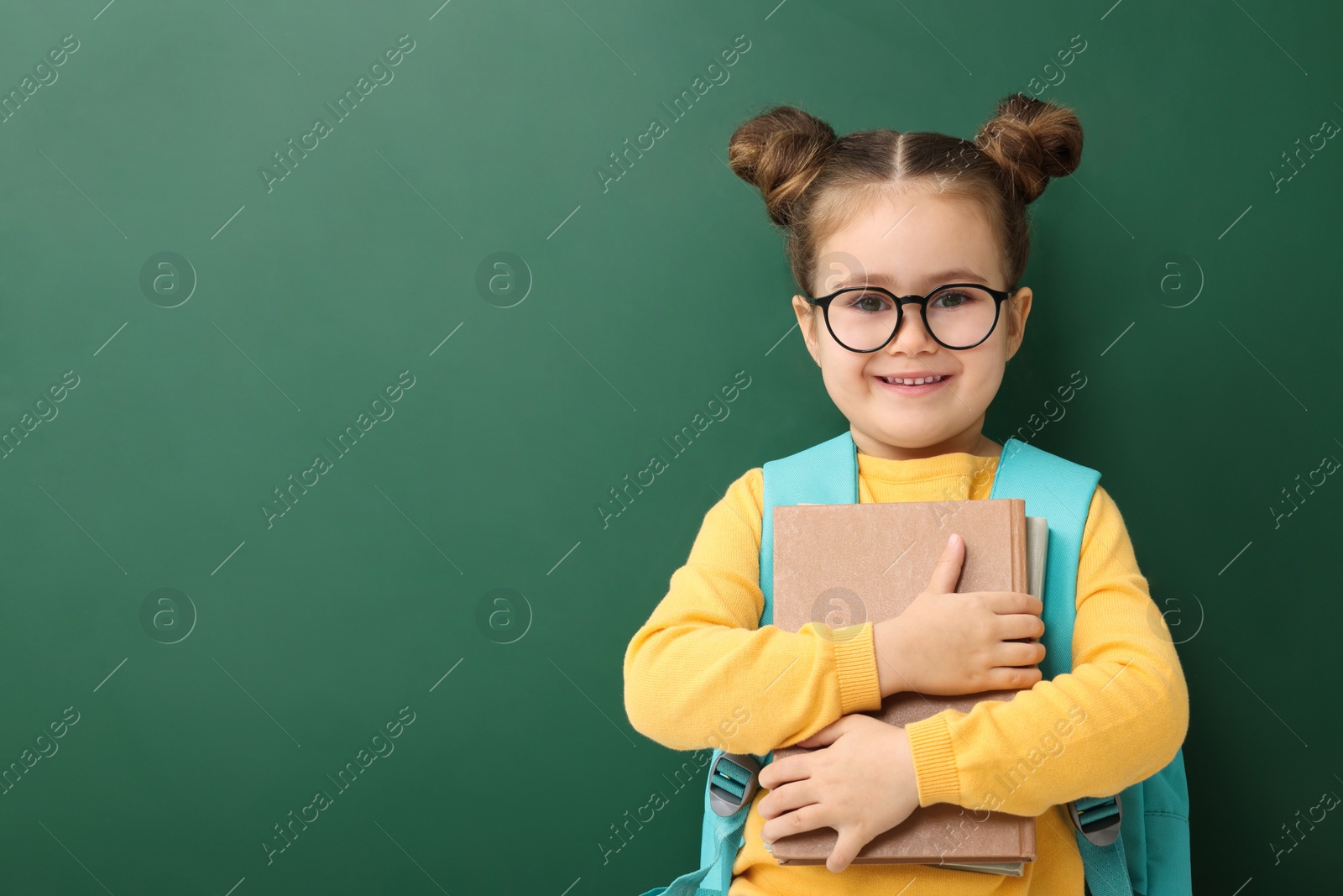 Photo of Happy little school child with notebooks near chalkboard. Space for text