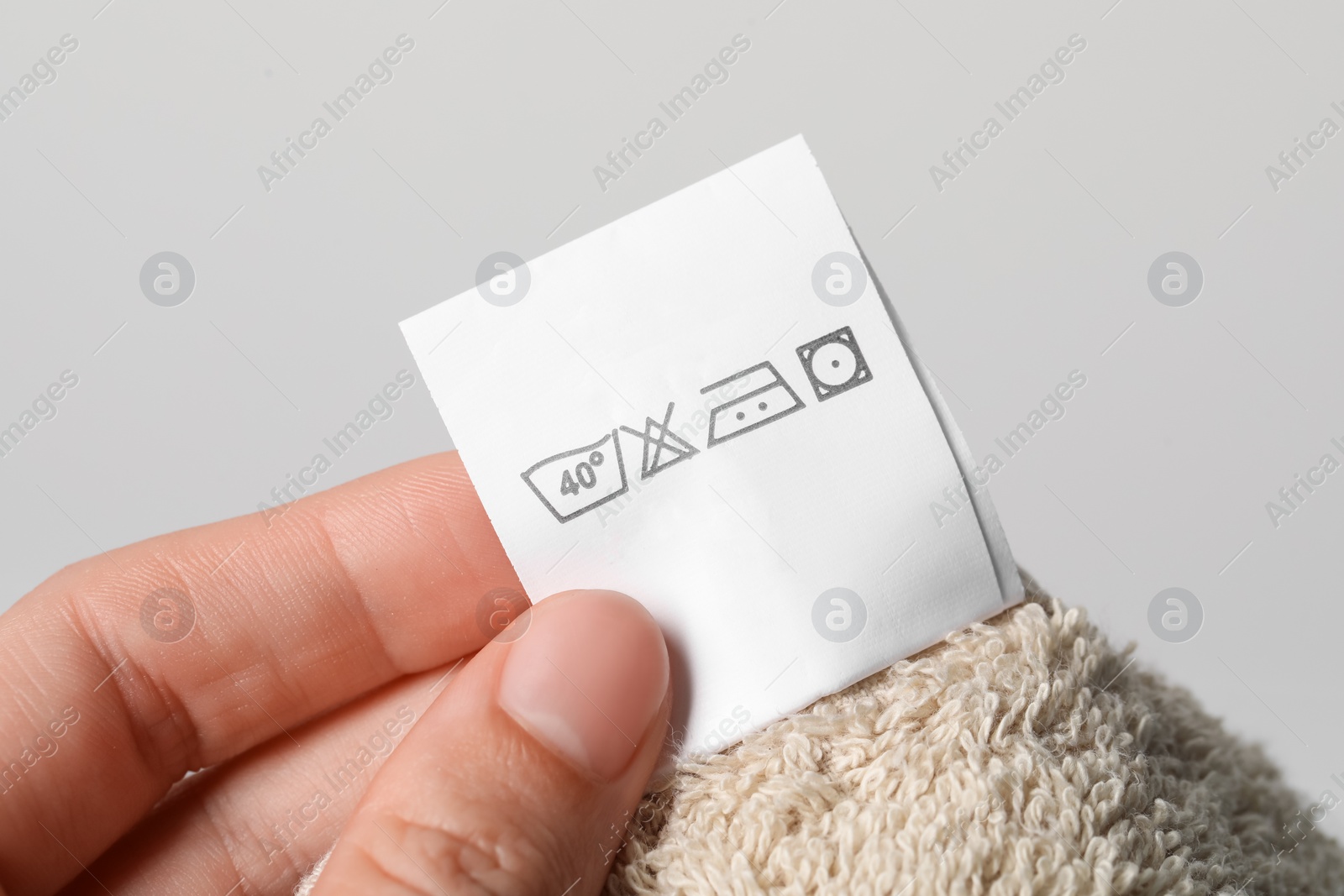 Photo of Woman holding clothing label on light brown towel, closeup