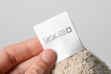 Photo of Woman holding clothing label on light brown towel, closeup