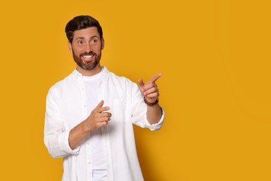 Photo of Smiling bearded man pointing forward fingers on orange background. Space for text