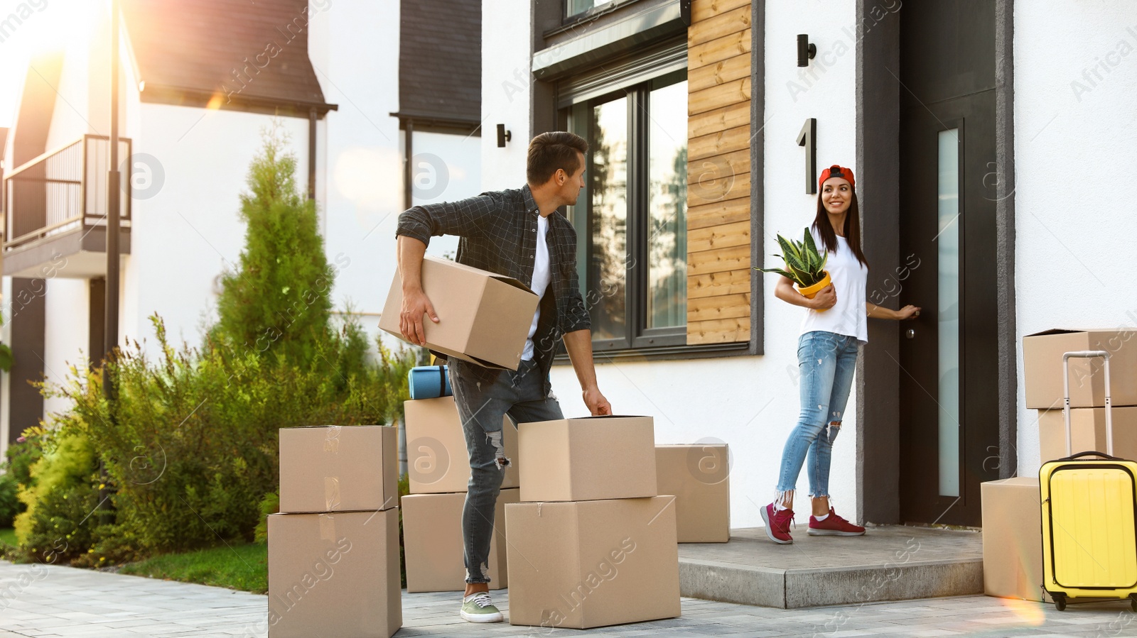 Photo of Happy couple with moving boxes and household stuff near their new house on sunny day