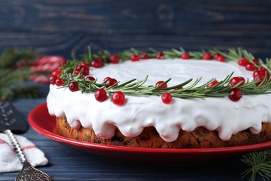 Traditional Christmas cake decorated with rosemary and cranberries on blue wooden table, closeup