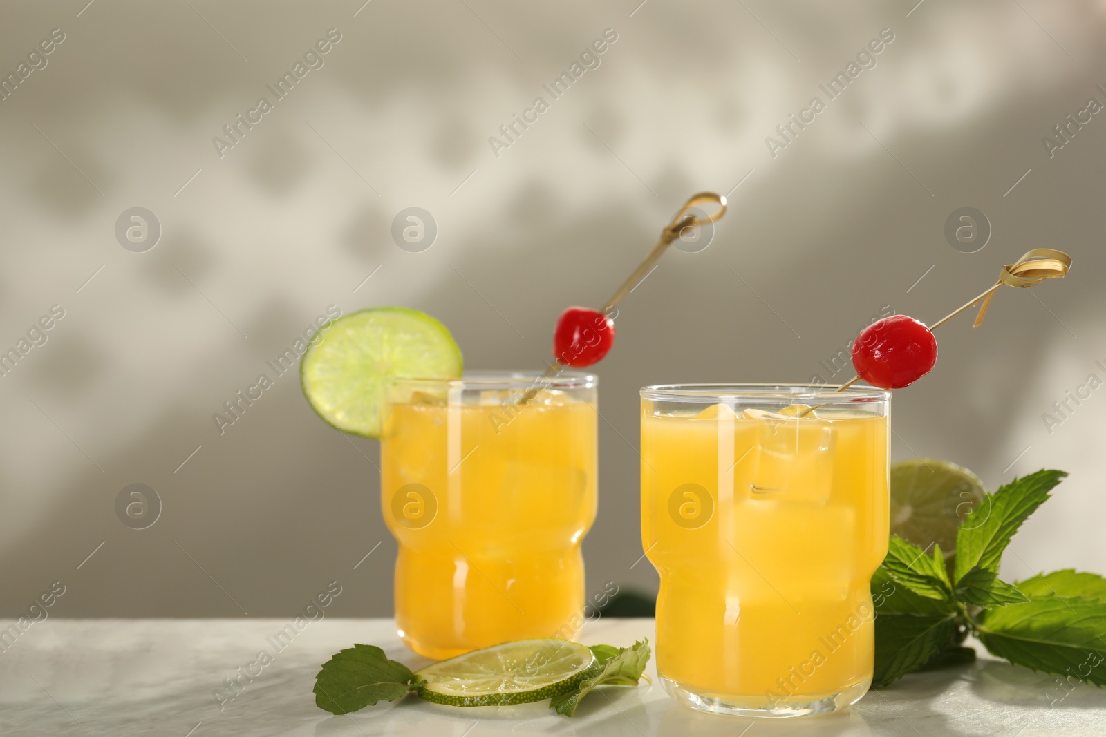 Photo of Glasses of tasty pineapple cocktail with cherry, lime and mint on white table. Space for text