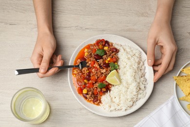 Photo of Woman with rice and chili con carne at white wooden table, top view