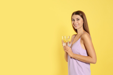 Photo of Young woman with glass of lemon water on yellow background. Space for text