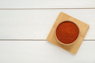 Bowl with aromatic paprika powder on white wooden table, top view. Space for text
